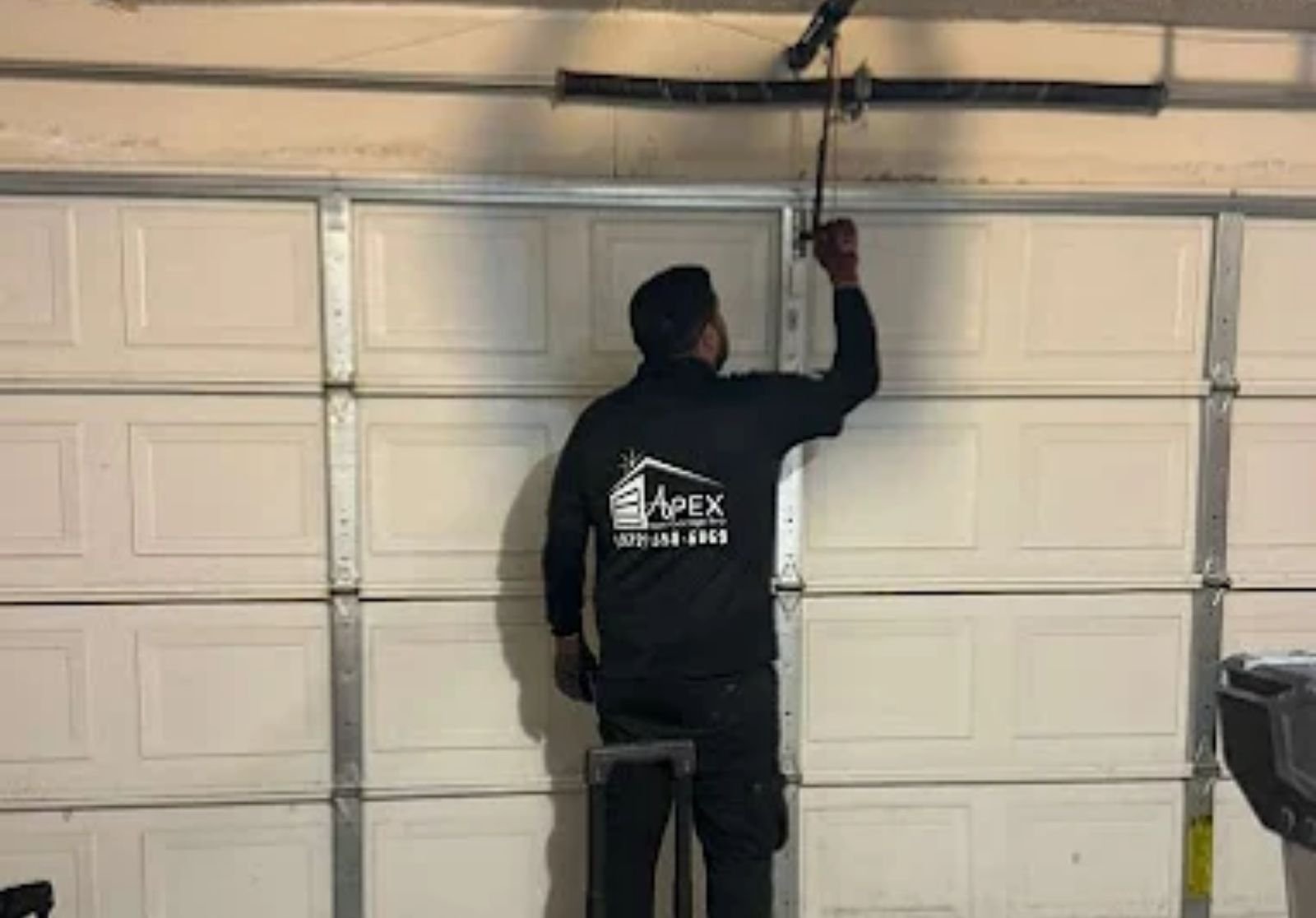 Technician repairing garage door track and cables on a white sectional door